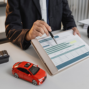Lawyer pointing at car loan or comparison document next to red toy car model.