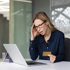 Stressed woman holding credit card at laptop dealing with identity theft or fraud legal issues.