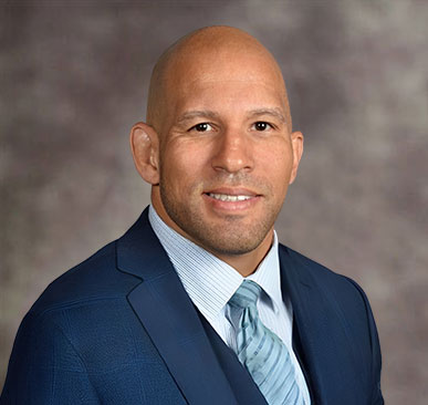 Headshot of a smiling bald man in a blue suit and tie, labeled Raphael Davis, Esq.